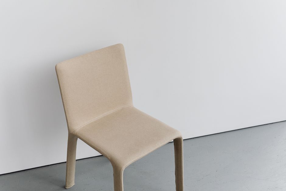 A minimalist beige chair against a white wall, ideal for elegant home interiors.